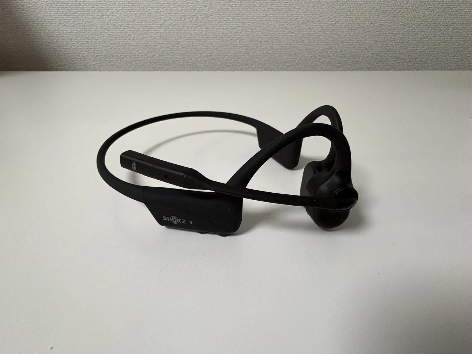 ブームマイクを上げた状態。マイクの上部に Shokz マークのミュートボタンとマイク穴、下の本体には SHOKZ ロゴと LED インジケーター