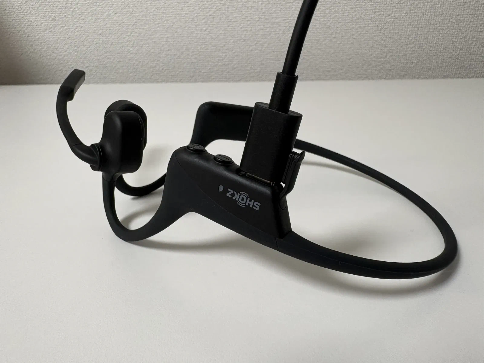充電中の OpenComm2。バンド裏の端子に USB-C ケーブルが挿さっている